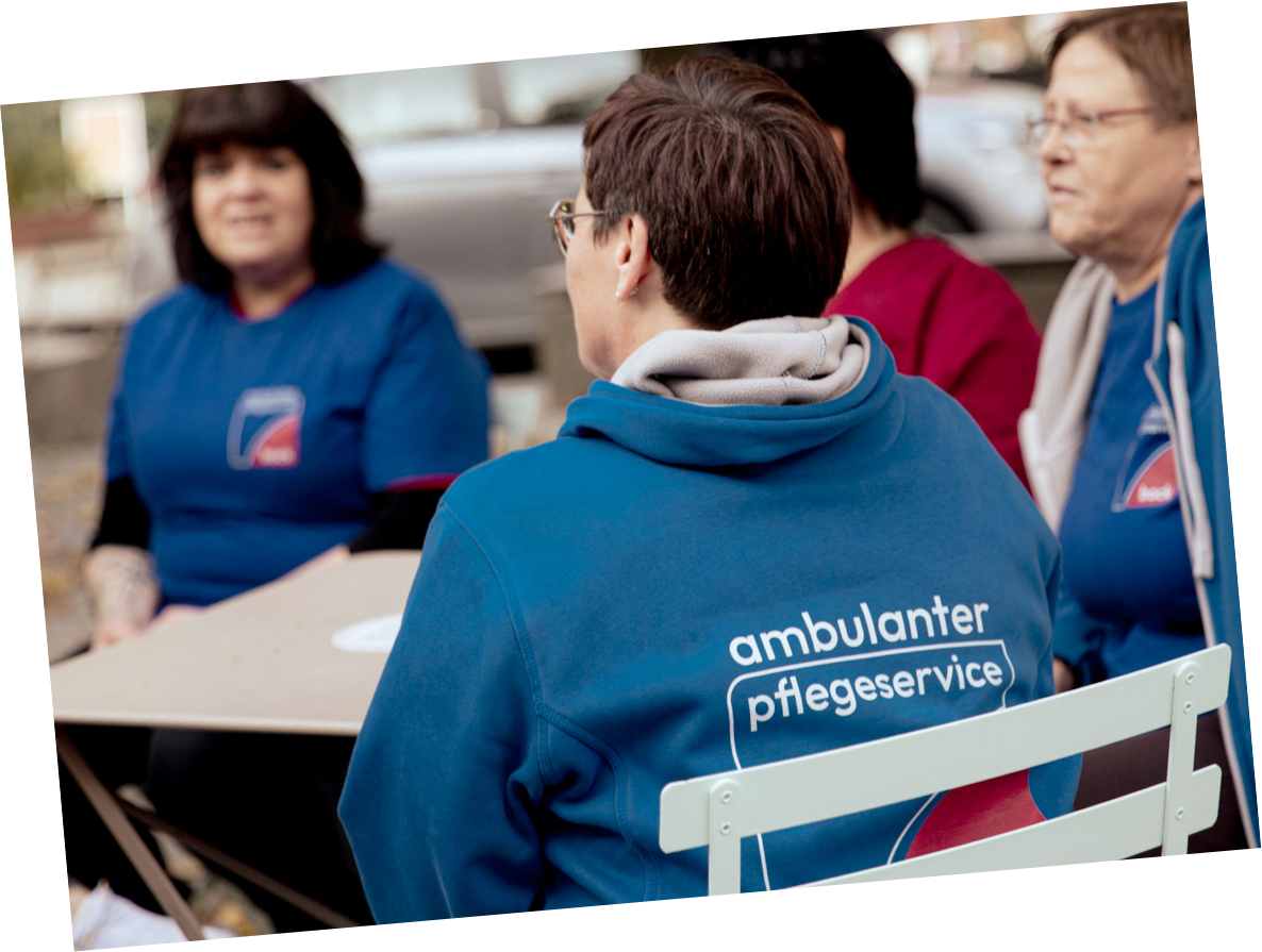 Teammitglieder vom ambulanten Pflegeservice sitzen mit Teamjacken an einem Tisch